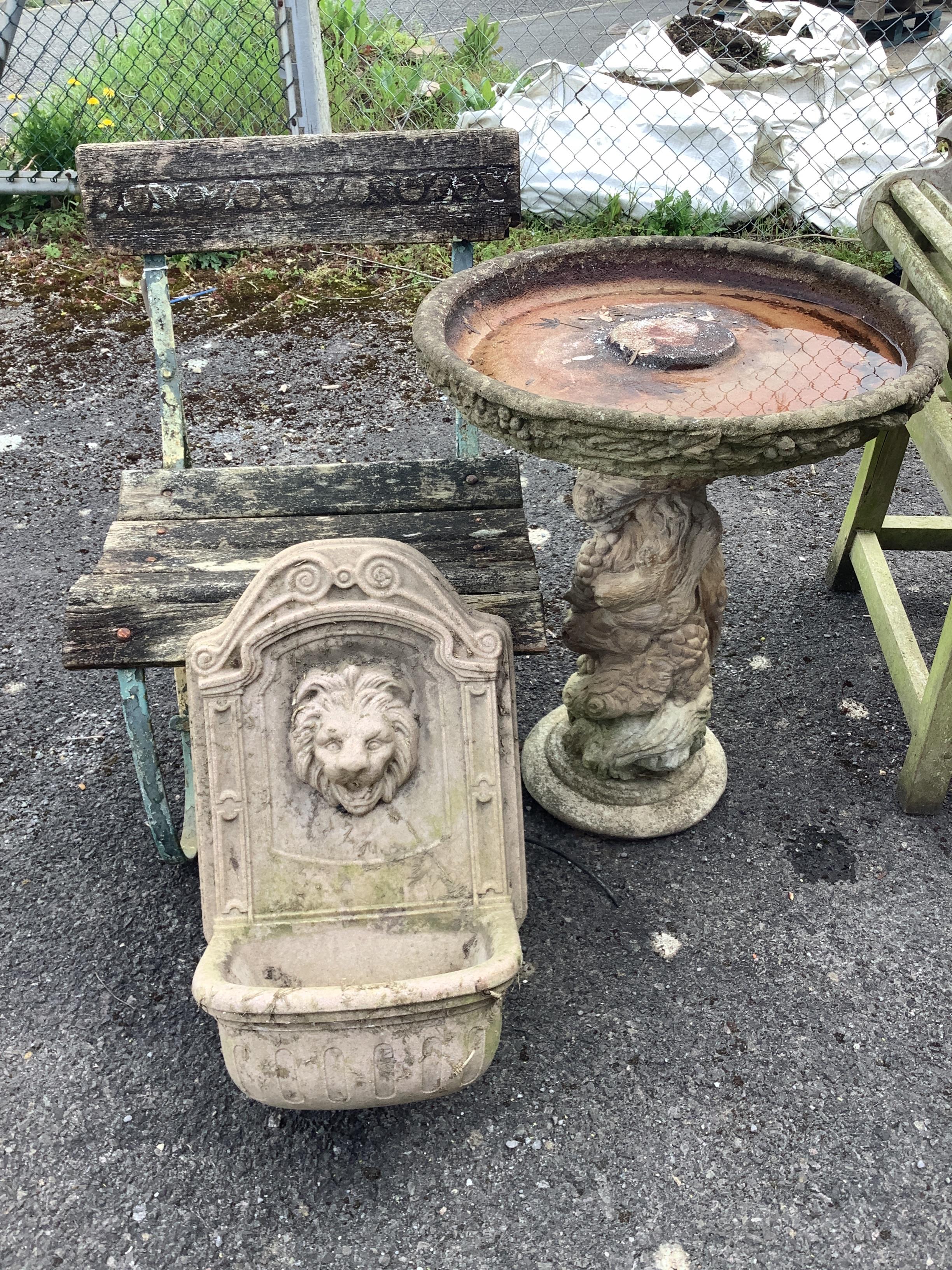 A composition faux marble lion mask wall fountain, a slatted wrought iron garden chair and a circular reconstituted stone bird bath